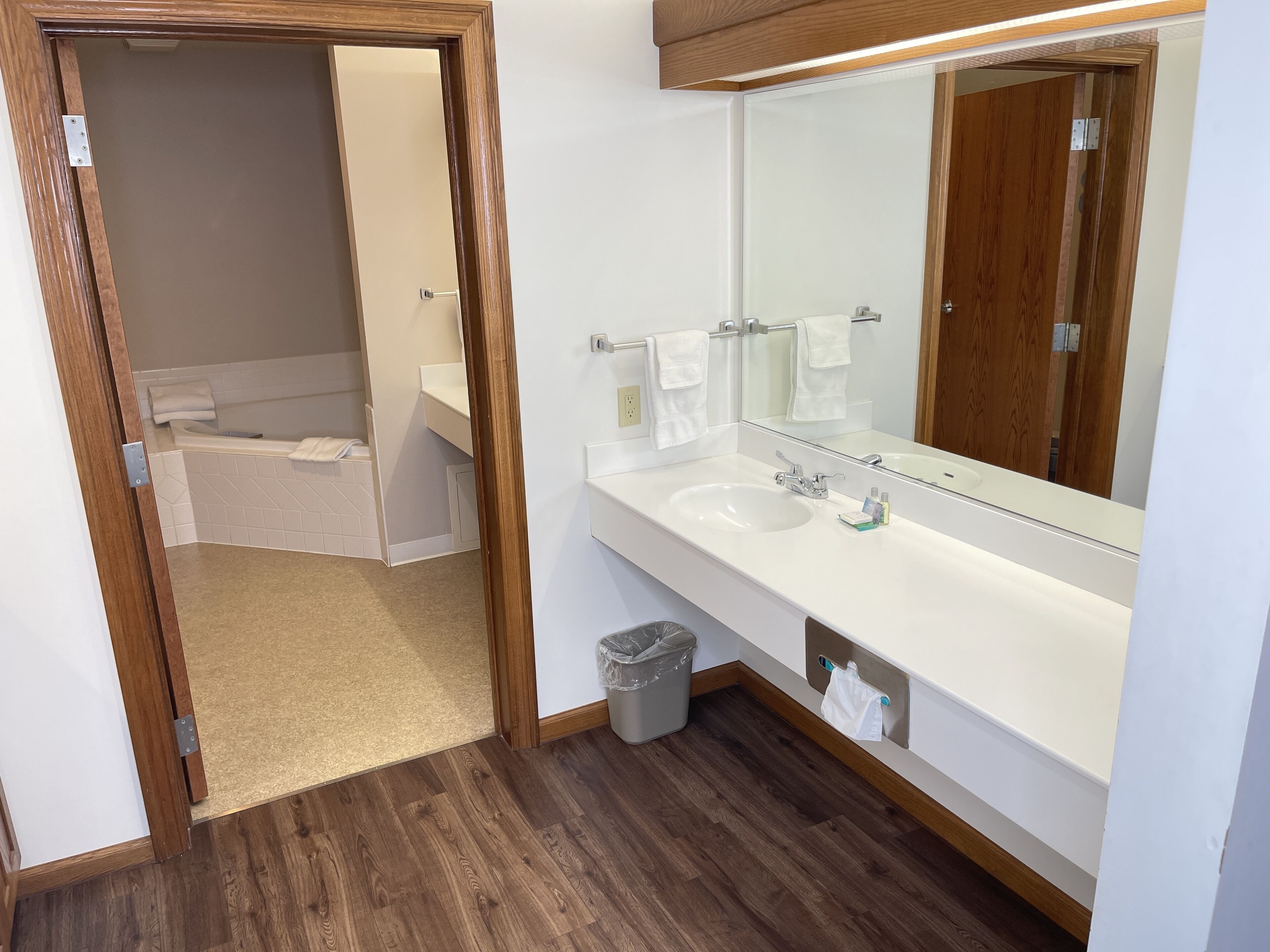 Une salle de bain moderne avec un plancher en bois, un lavabo blanc, un grand miroir et une baignoire.