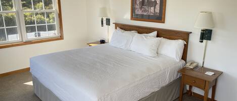 Una cama bien hecha con sábanas blancas, cabecera de madera y dos mesitas de noche con lámparas y un teléfono.