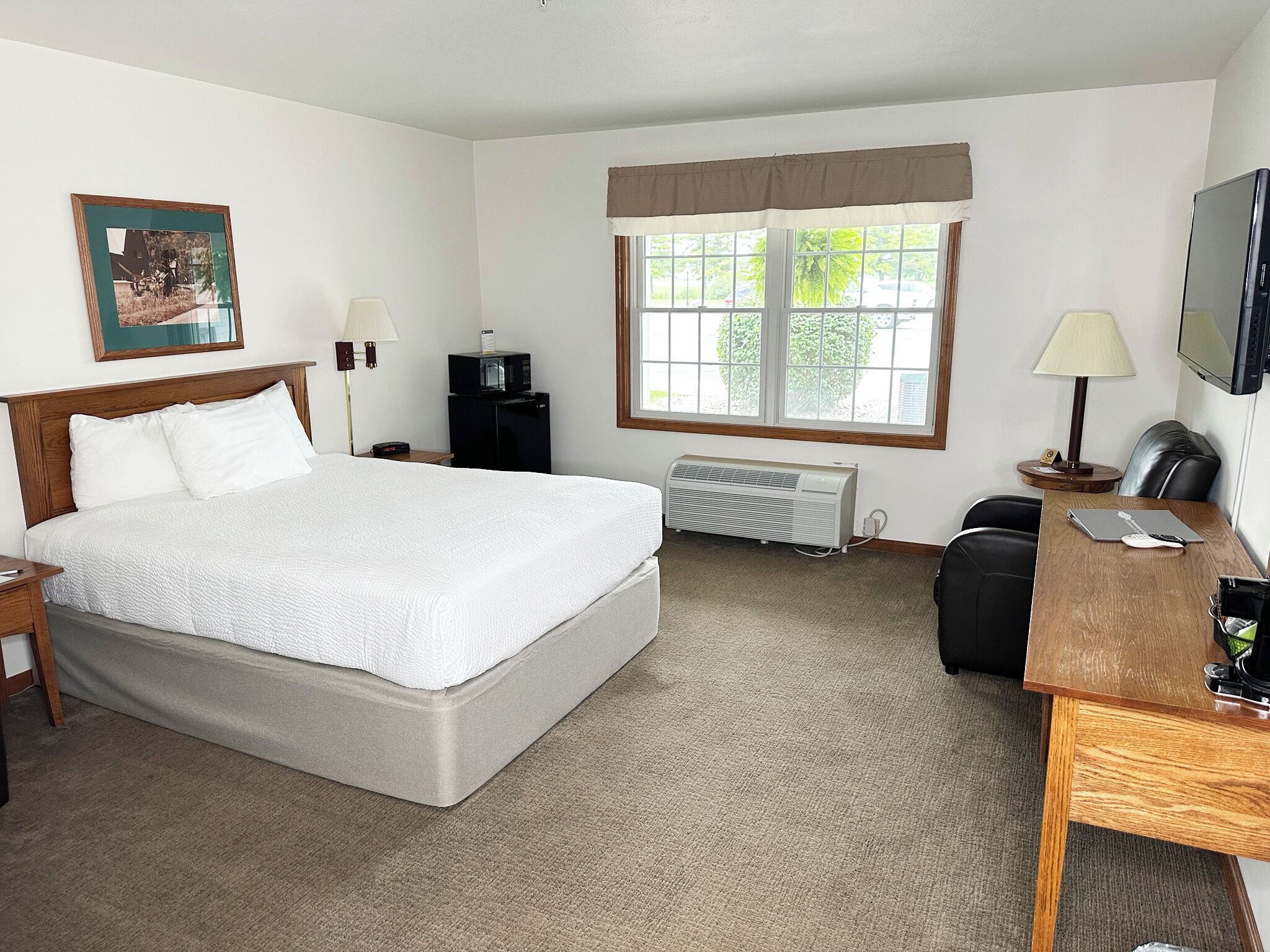 Habitación de hotel con una cama grande, un escritorio con silla, televisor, calentador y ventana con cortinas.