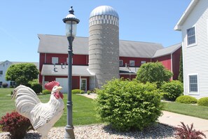 A rooster statue, a silo, and a red barn with a white house in the background.