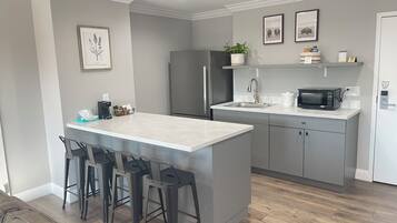 A modern kitchen with a central island, bar stools, a refrigerator, a microwave, and a sink.
