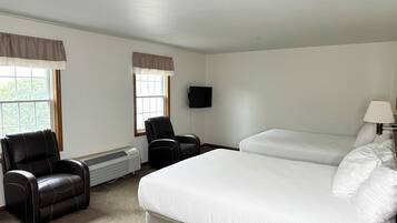 Una habitació d'hotel amb un llit gran, dues cadires, un televisor i una finestra amb cortines.