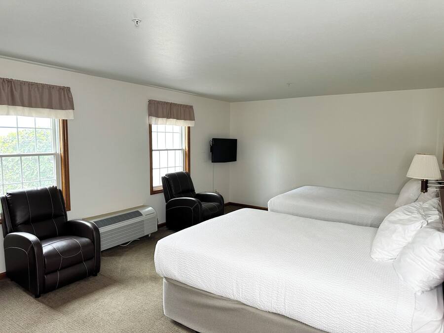 Una habitació d'hotel amb un llit gran, dues cadires, un televisor i una finestra amb cortines.