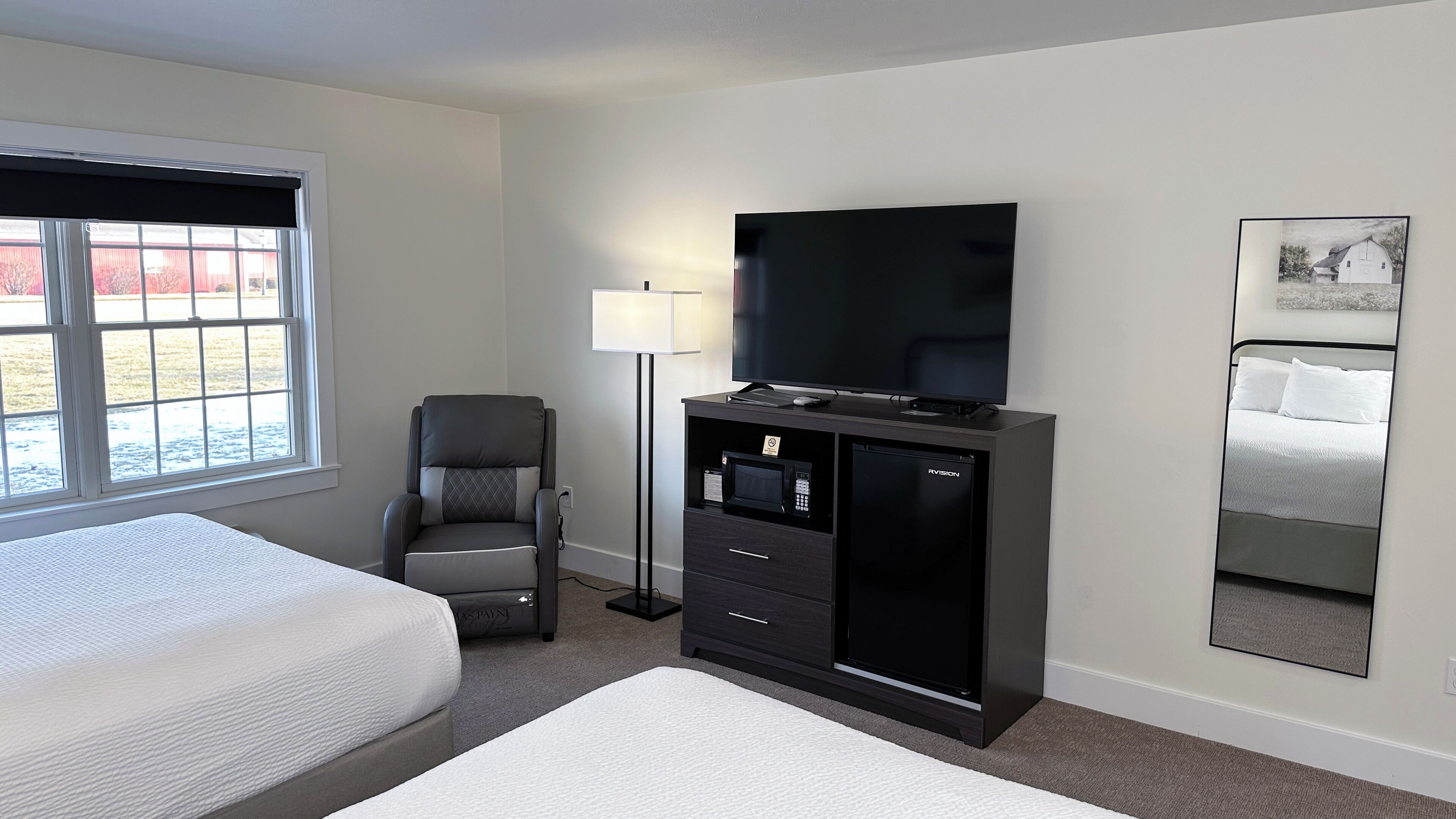 Habitación de hotel con cama, escritorio con televisor de pantalla plana, silla, lámpara y un espejo grande.