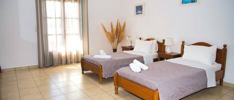 Habitación de hotel con dos camas de madera, un ventanal con cortinas, un jarrón con plumas de pampa y un cuadro pequeño en la pared.