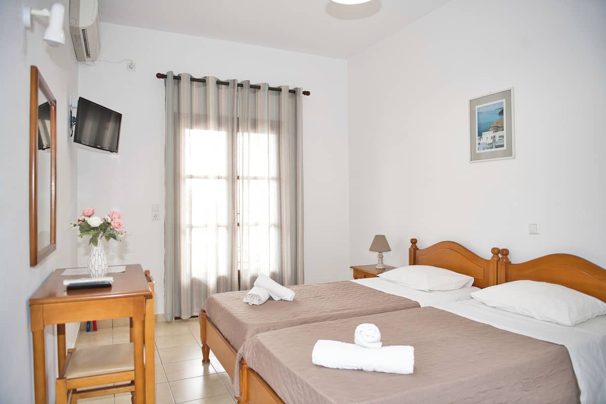 A hotel room with two beds, a desk with a lamp, a TV, and a window with curtains.