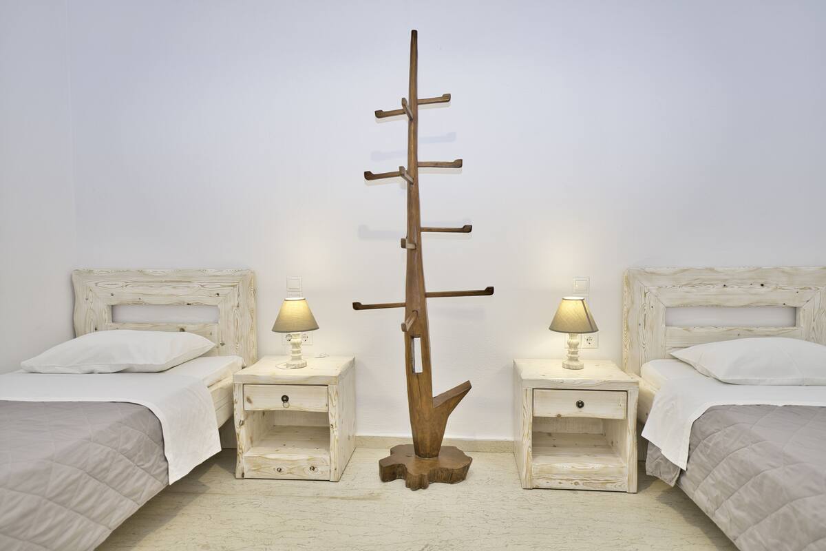 A bedroom with two beds, each with a nightstand and a lamp. A wooden ladder is placed between the beds.