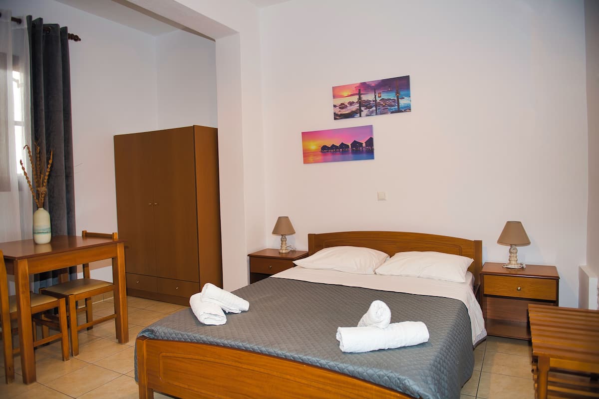 A hotel room with a bed, two nightstands, a wooden desk, a chair, a wardrobe, and two wall art pieces.