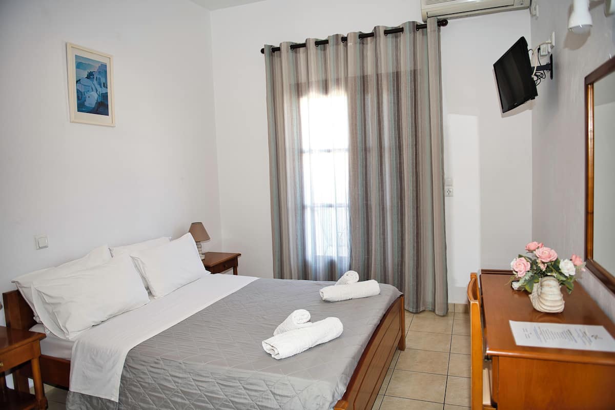 A hotel room with a bed, a desk, a chair, a TV, and a window with curtains.
