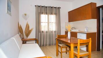 A compact living space with a sofa, dining table, chairs, a kitchen area with cabinets, and a window with curtains.