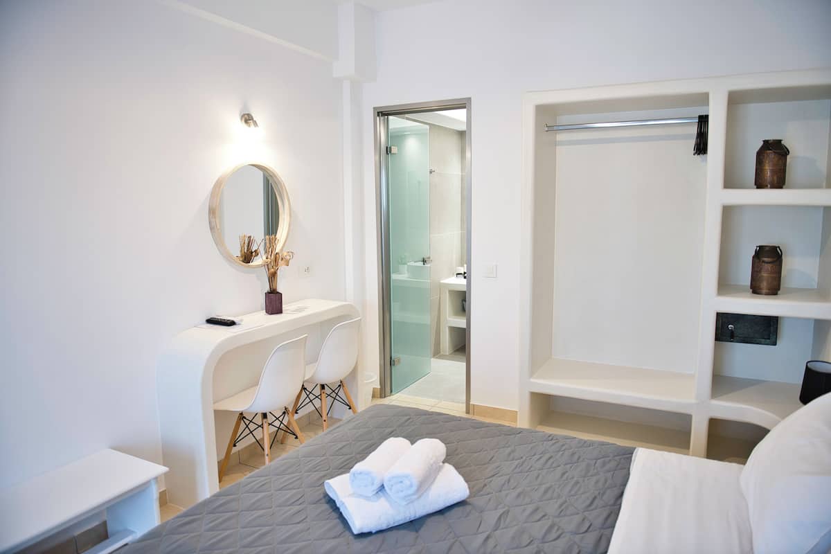 A hotel room with a bed, a desk with a chair, a wardrobe, and a bathroom visible through an open door.