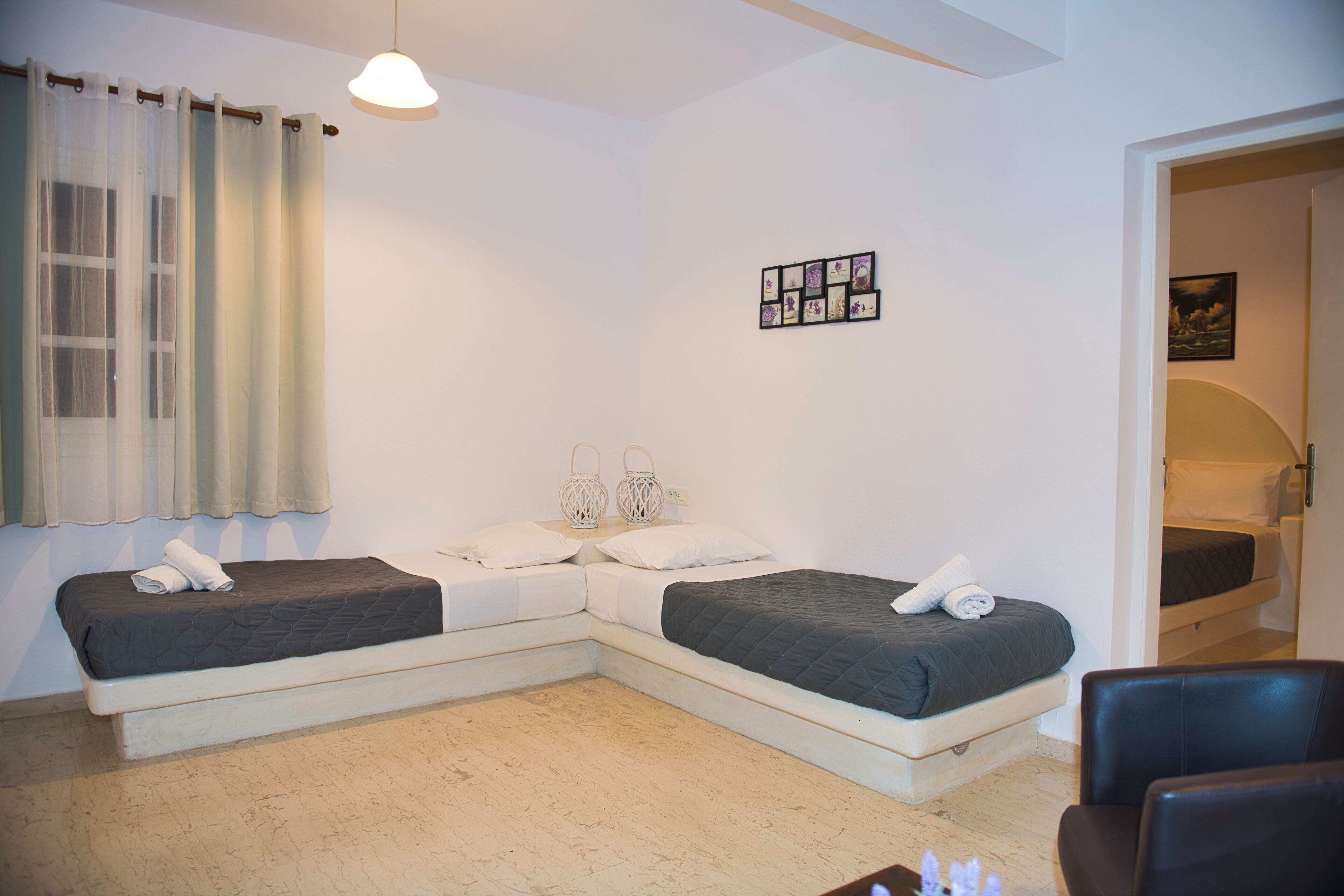 A room with two beds, a chair, a hanging light, and a wall-mounted picture.