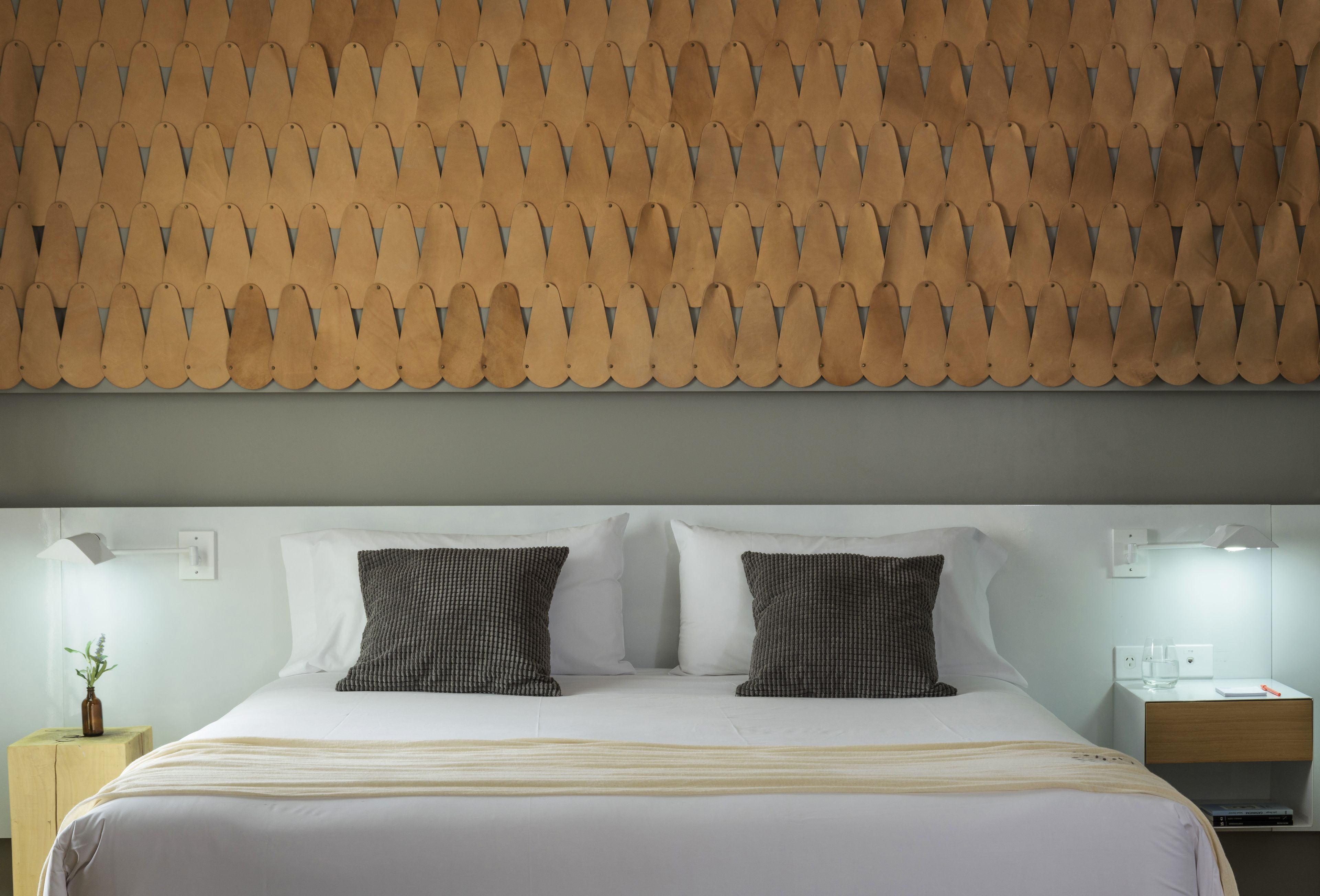 Una cama bien tendida con sábanas blancas y dos almohadas, un cabecero de madera con diseño festoneado y mesitas de noche con lámparas.