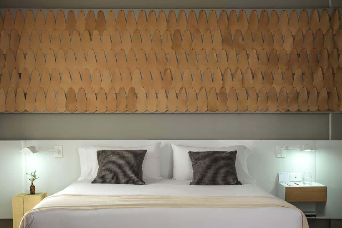 Une chambre moderne avec un grand lit, deux tables de chevet, une petite table et un mur décoré d’un motif placé au-dessus du lit.