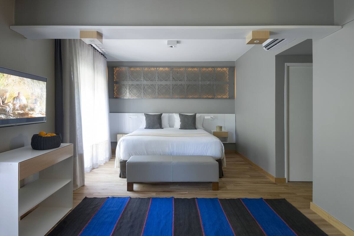 Une chambre moderne avec un grand lit, un téléviseur sur le côté gauche et un plancher en bois.