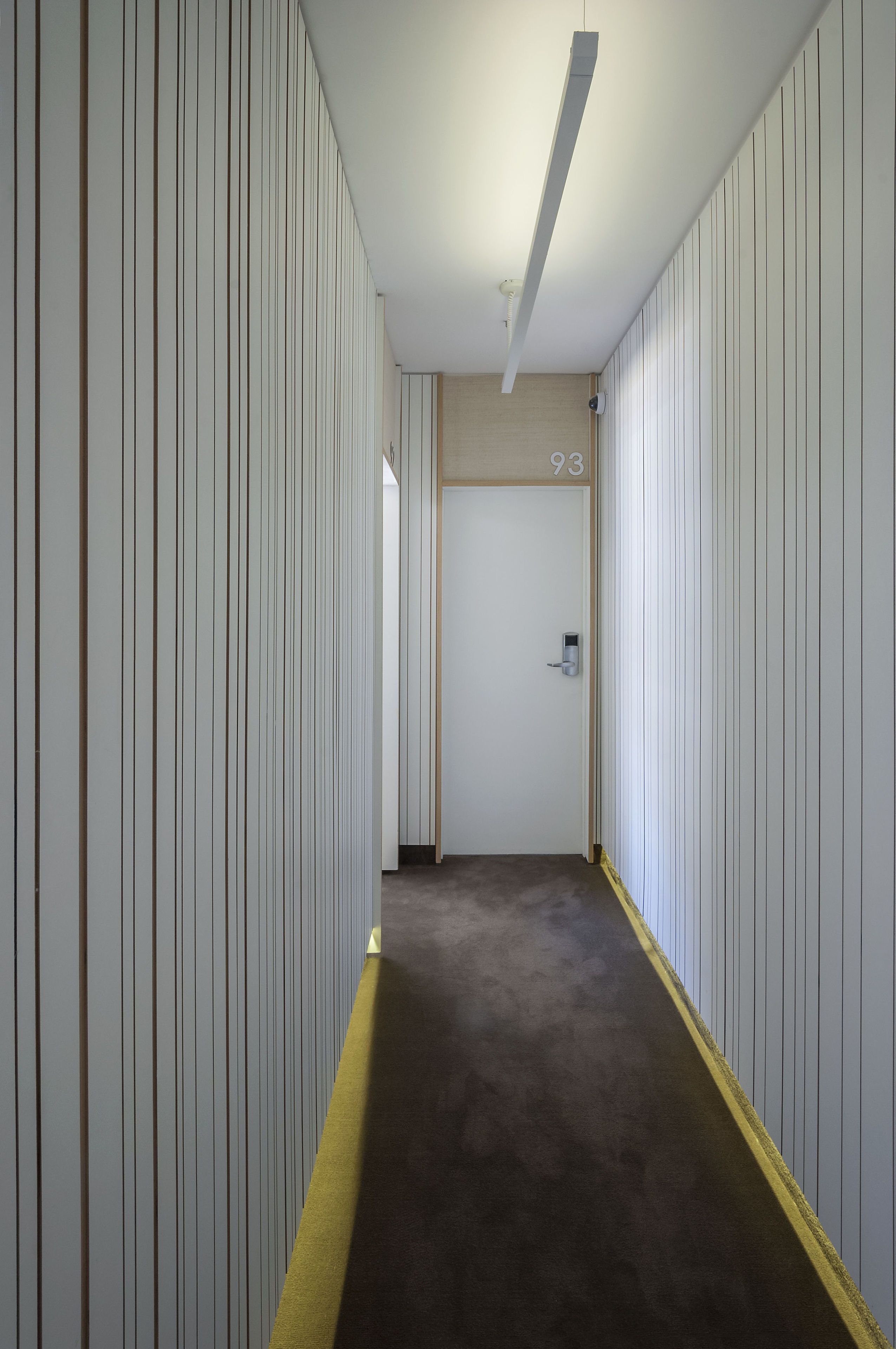 A narrow hallway with vertical paneling on the walls, a carpeted floor, and a door labeled "93" at the end.