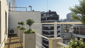 Terraza en la azotea con suelo de madera, macetas de concreto con plantas y vistas de edificios circundantes.