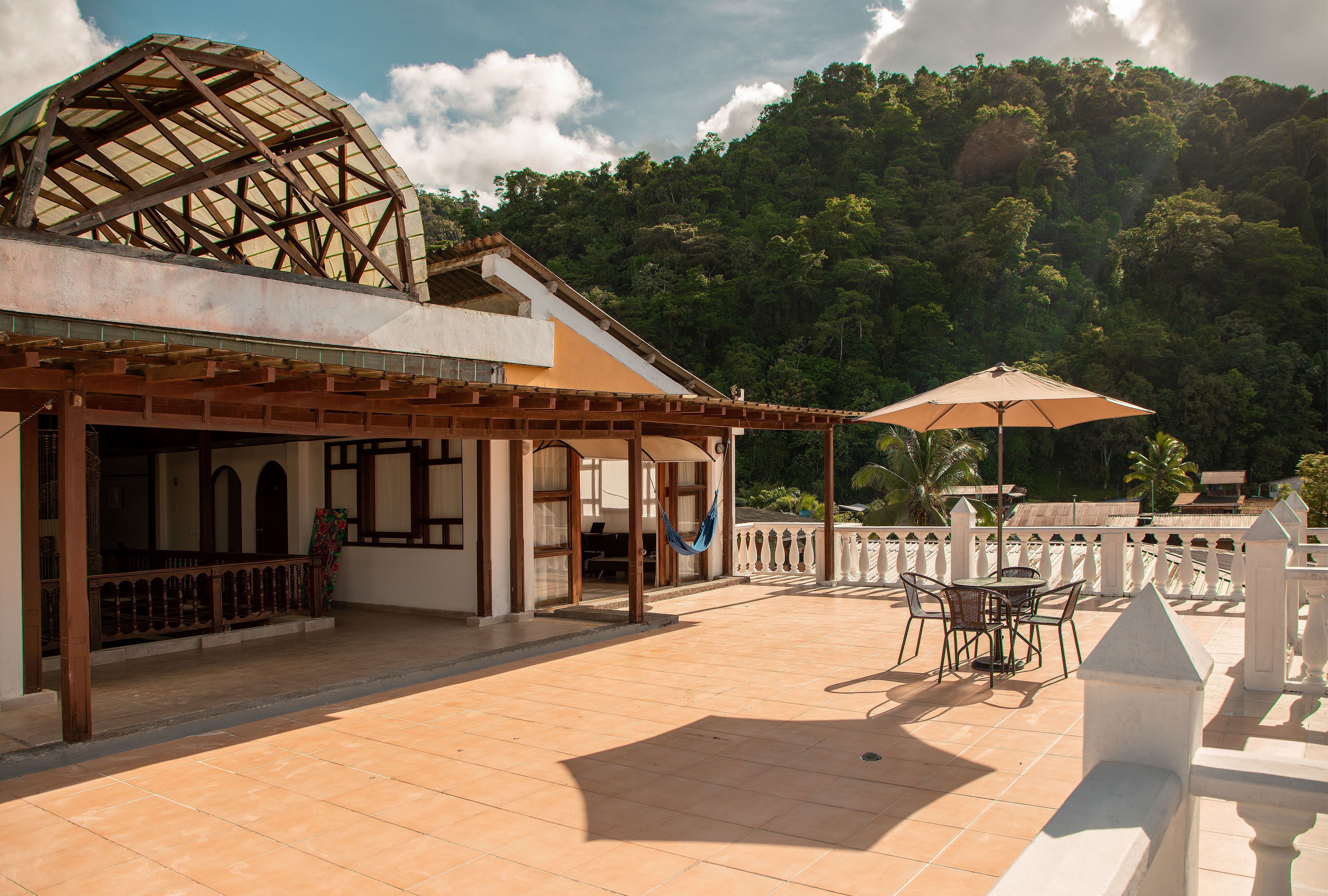 A terrace with a table and chairs, a hammock, and a view of a forested hill.