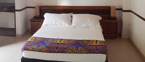 Un dormitorio con cama, cabecera de madera, mesitas de noche y un techo con vigas de madera.