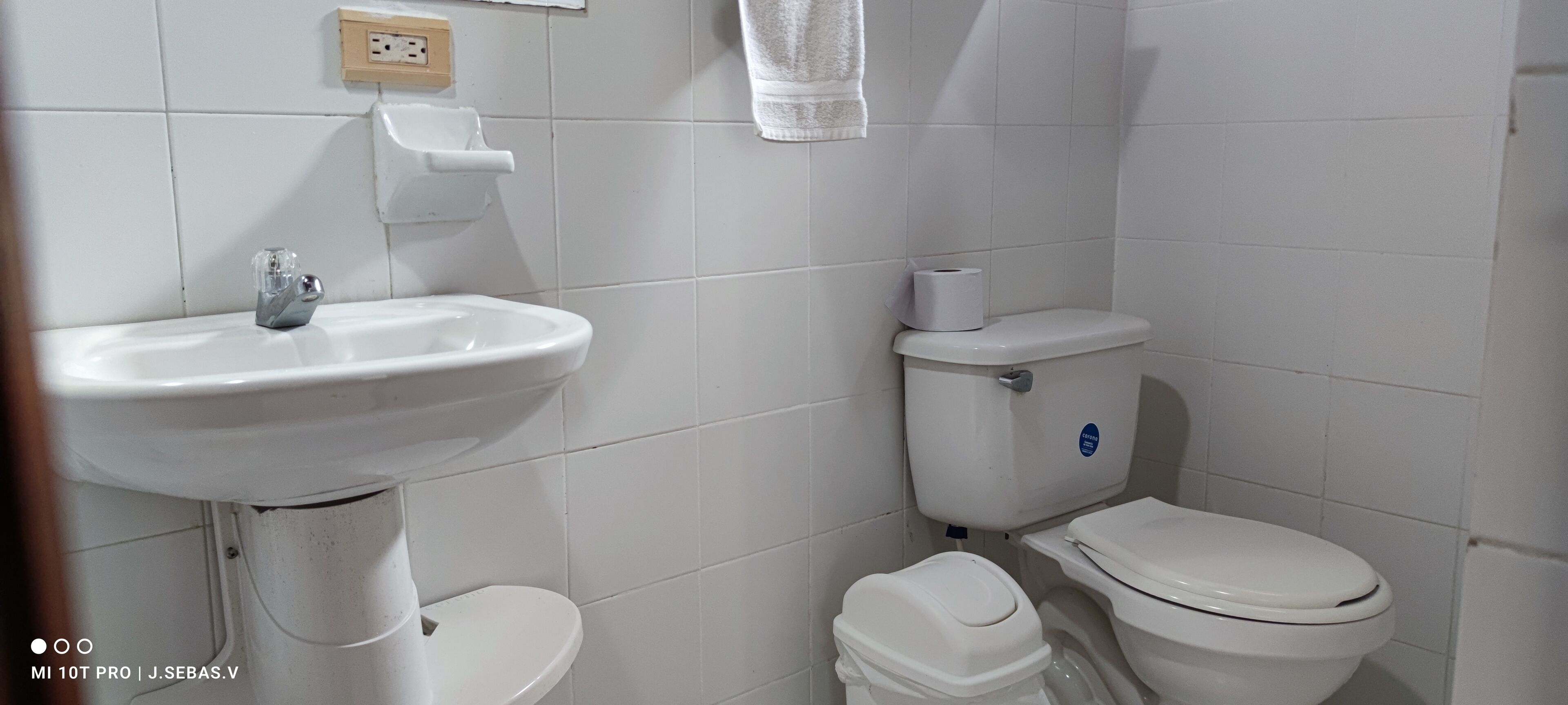 A bathroom with a white sink, toilet, and a small trash bin.