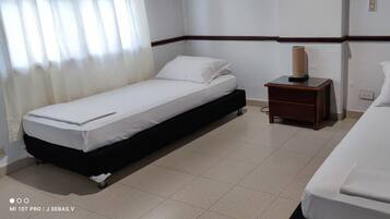 A hotel room with two single beds, a wooden nightstand with a lamp, and a tiled floor.
