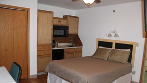 A bedroom with a bed, a small kitchenette, and a wooden door.