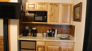 A compact kitchen with wooden cabinets, a microwave, a coffee maker, and a sink.
