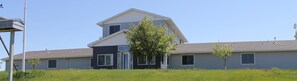 A modern two-story house with a flat roof, large windows, and a small front yard with young trees.