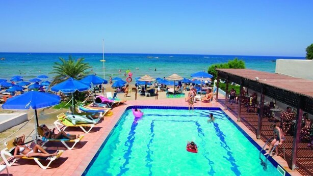 A pool area with lounge chairs and umbrellas, a swimming pool, and a view of the ocean. - Stalis Hotel (Hersonissos)