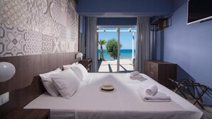 A hotel room with a bed, a nightstand, a TV, and a view of the beach. - Stalis Hotel (Hersonissos)