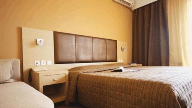 A hotel room with a large bed, a bedside table, a nightstand, and a wall-mounted air conditioning unit.
