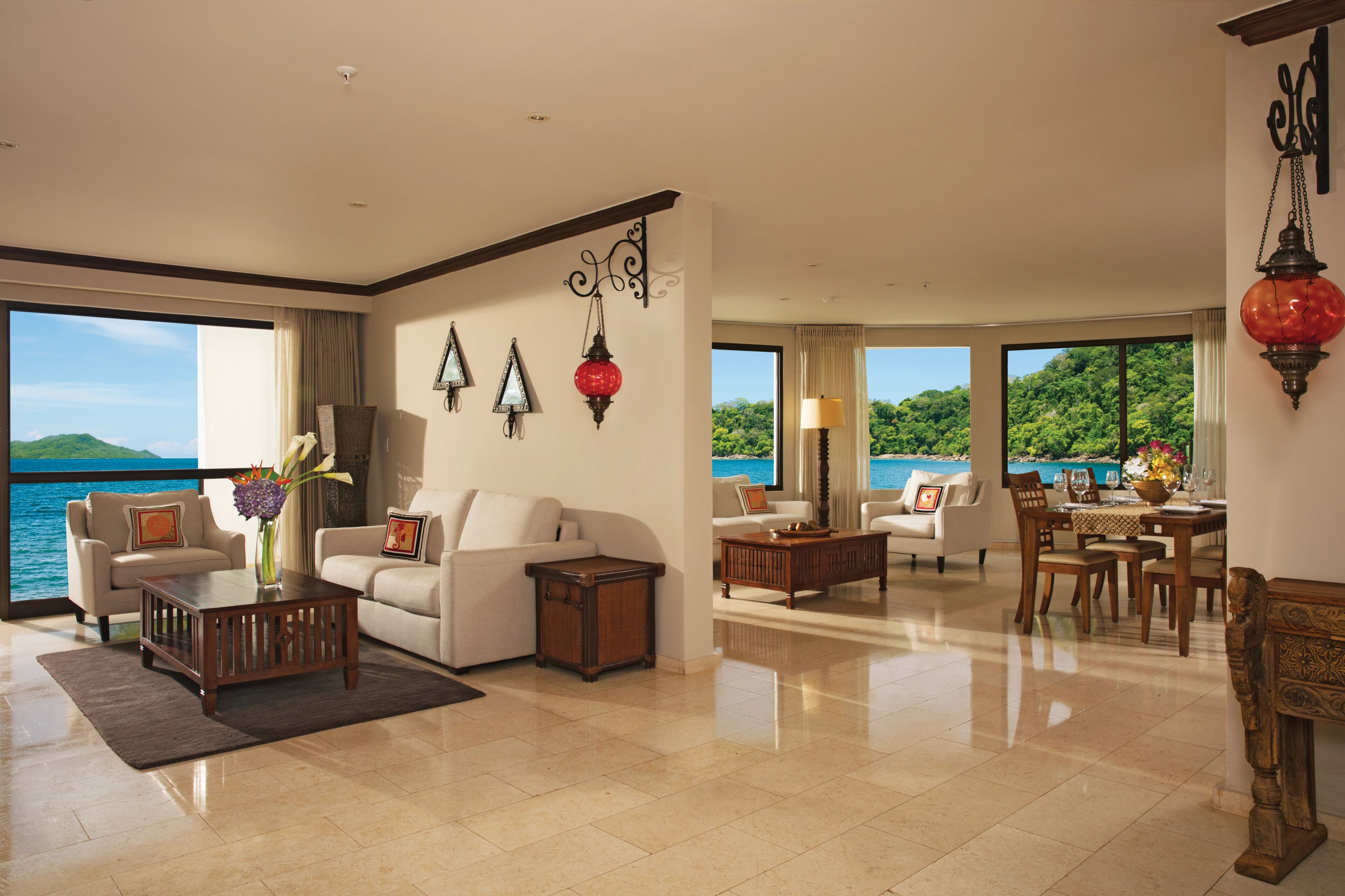 A spacious living room with a large window offering a view of the sea, a dining area with a table set for four, and a cozy seating area with two sofas and a coffee table.