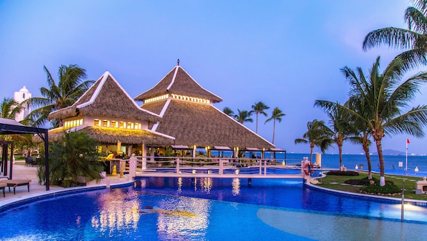 A resort with a large swimming pool, thatched-roof structures, and palm trees. - Dreams Playa Bonita Panama - All Inclusive (Veracruz)