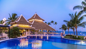 A resort with a large swimming pool, thatched-roof structures, and palm trees.
