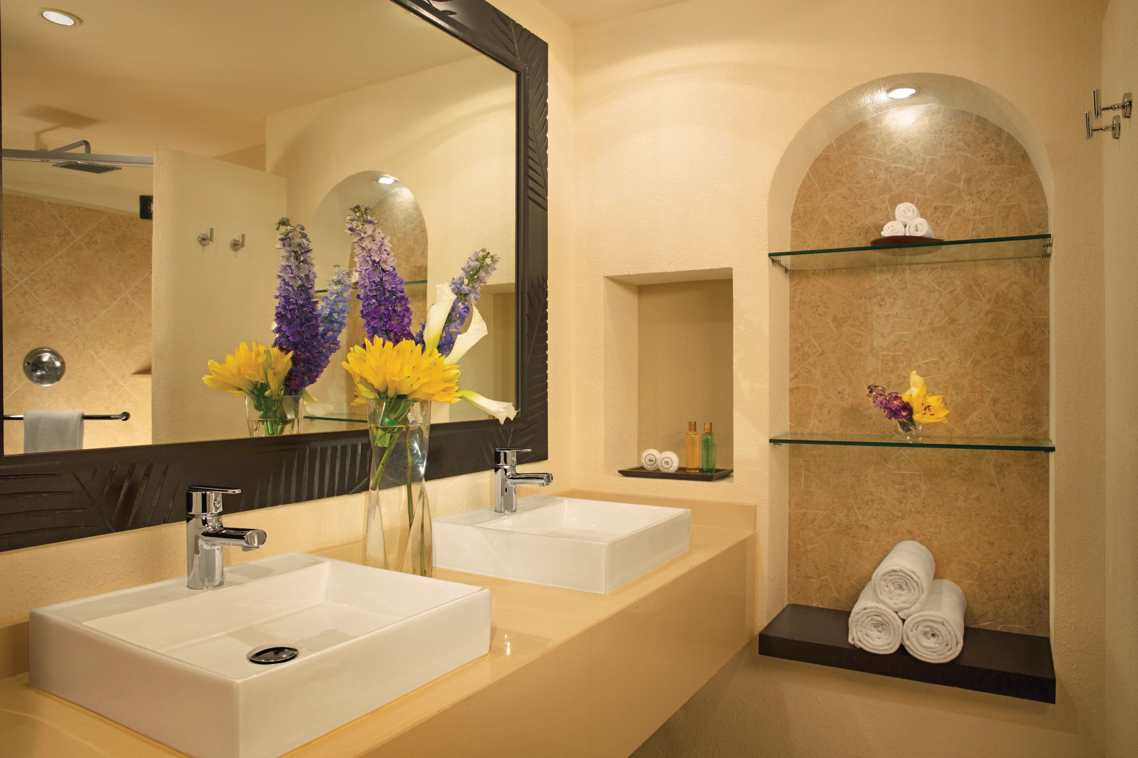 A bathroom with two sinks, a large mirror, and shelves with towels and toiletries.