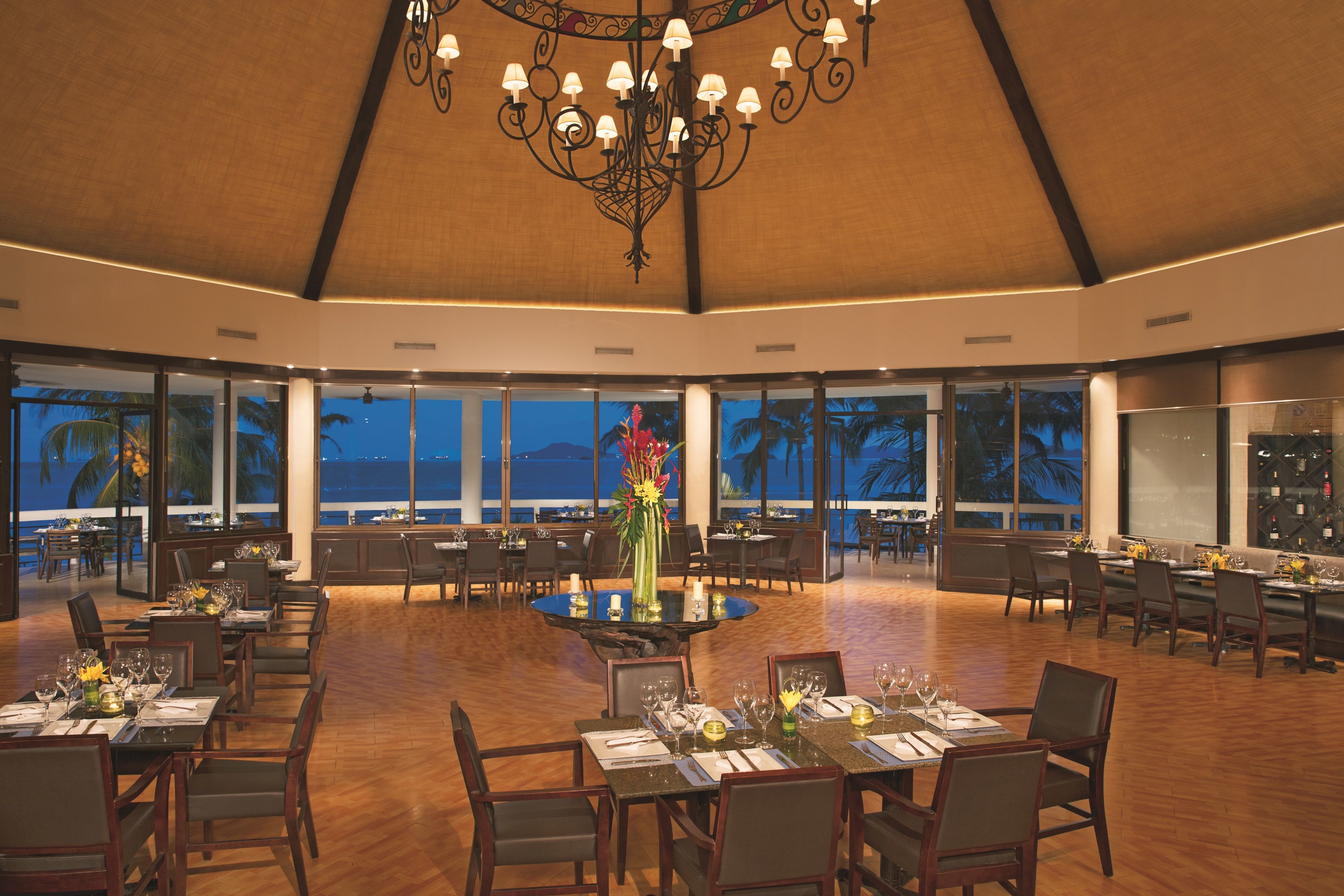 A spacious dining area with a high ceiling and large windows overlooking the ocean.