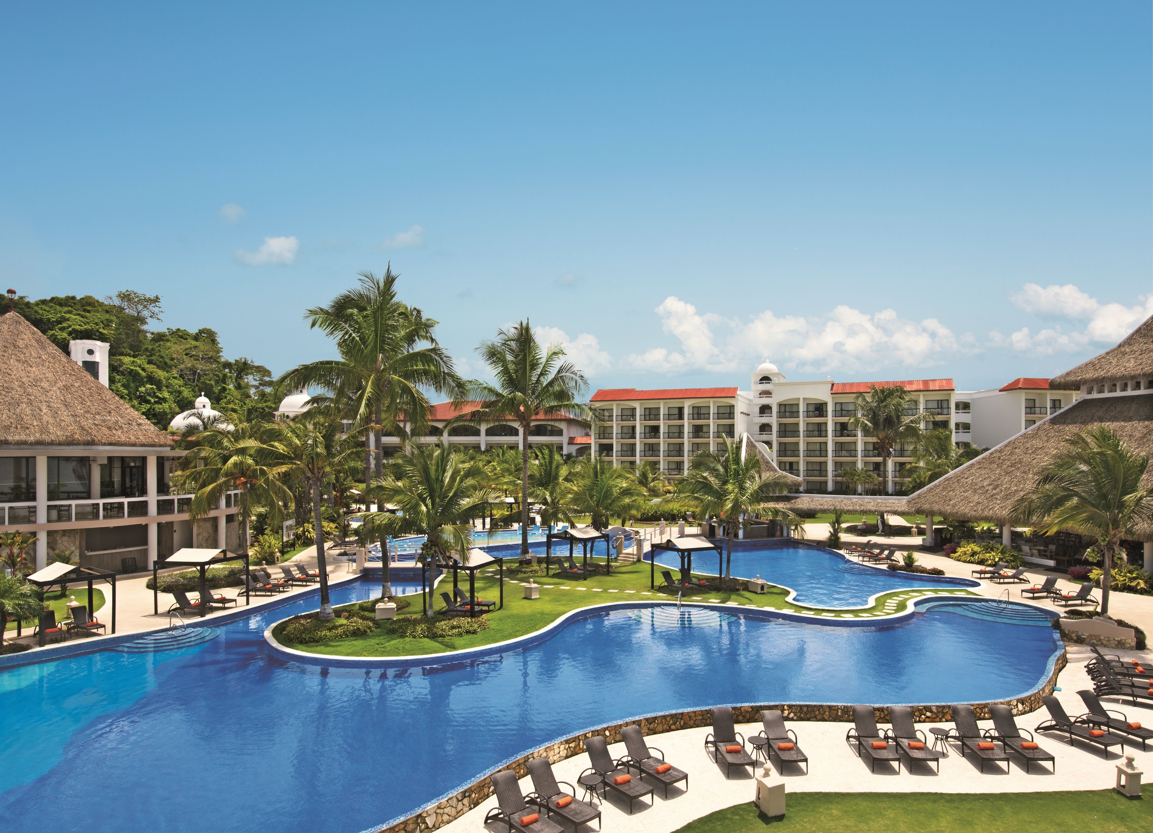 A resort with a large swimming pool, palm trees, and a building with a red roof.