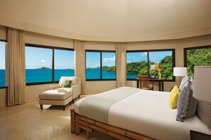 A hotel room with a large bed, a chair, a desk, and a view of the ocean. - Dreams Playa Bonita Panama - All Inclusive (Veracruz)