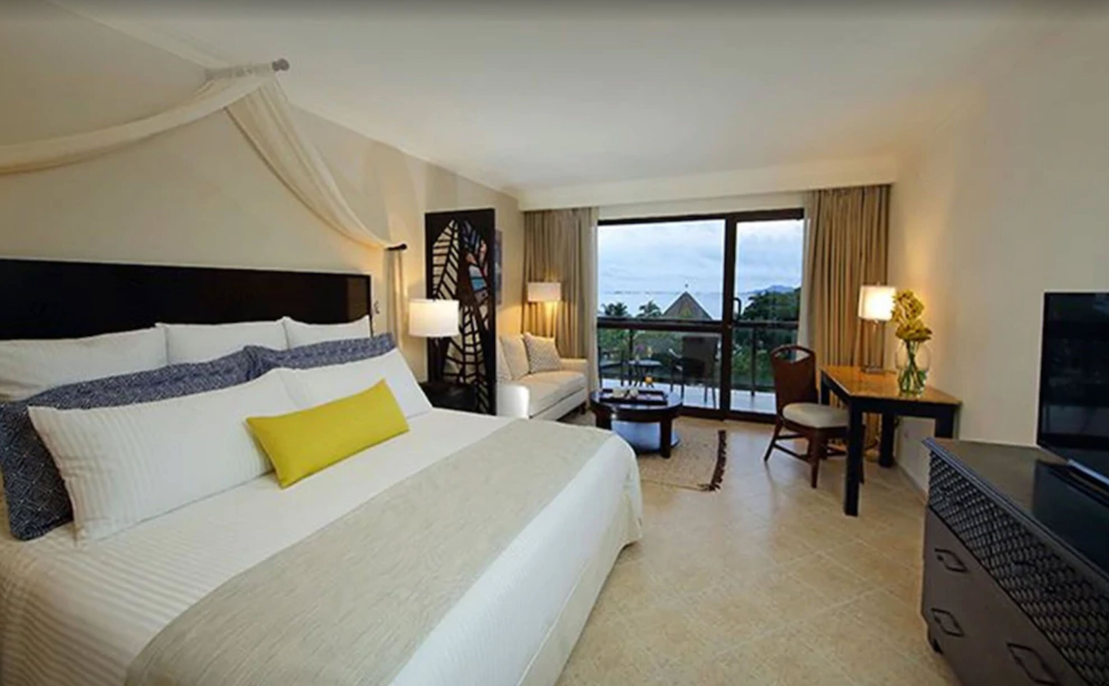A hotel room with a large bed, a desk, a chair, and a television.