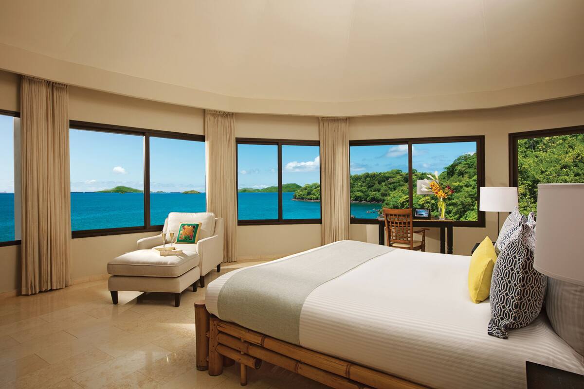 A hotel room with a large bed, a chair, a desk, and a view of the ocean.