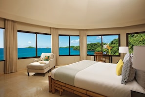 A hotel room with a large bed, a chair, a desk, and a view of the ocean.