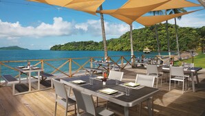 An outdoor dining area with tables and chairs, overlooking a body of water and a forested island. - Dreams Playa Bonita Panama - All Inclusive (Veracruz)