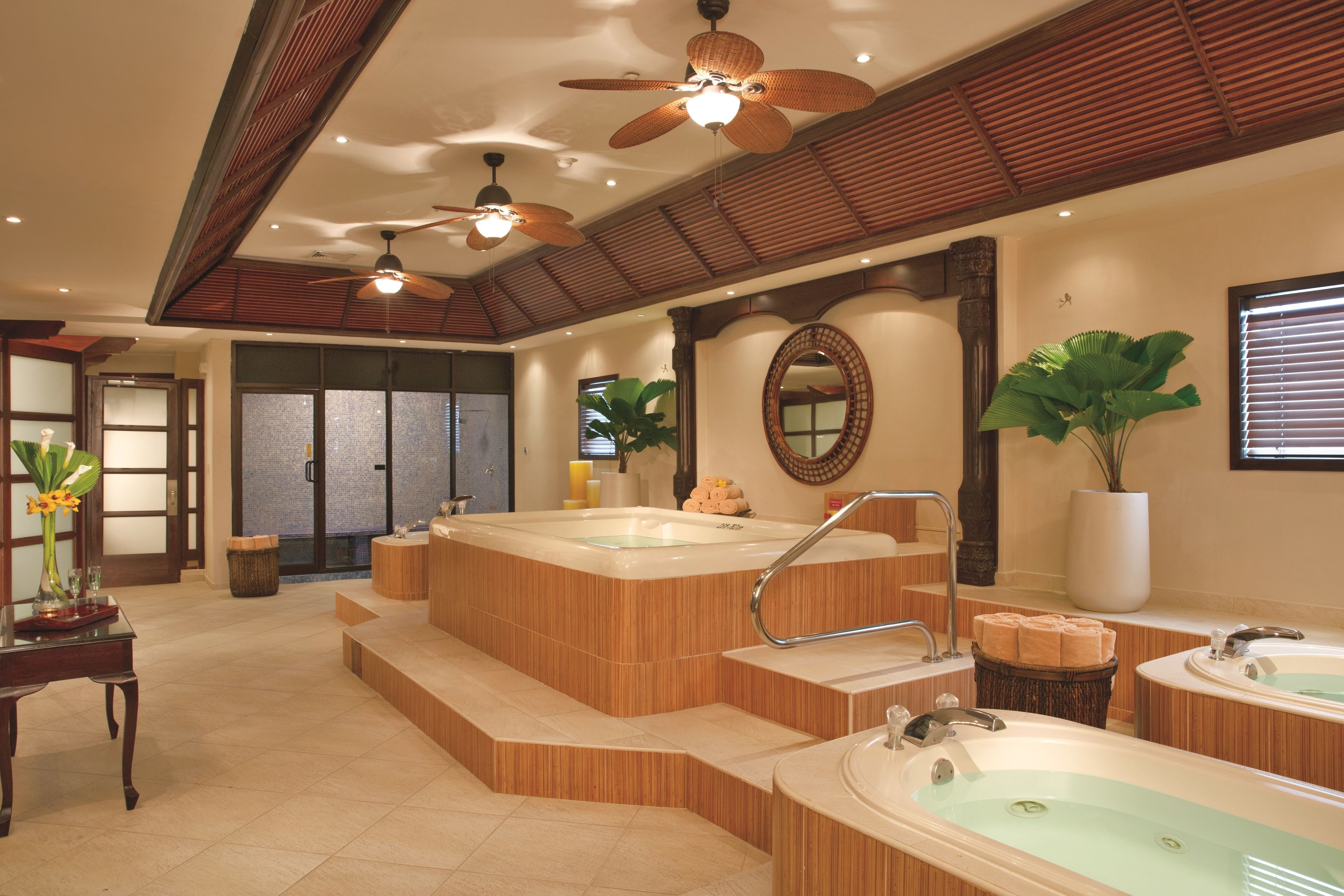 A spa area with multiple hot tubs, wooden steps, ceiling fans, and a large mirror.