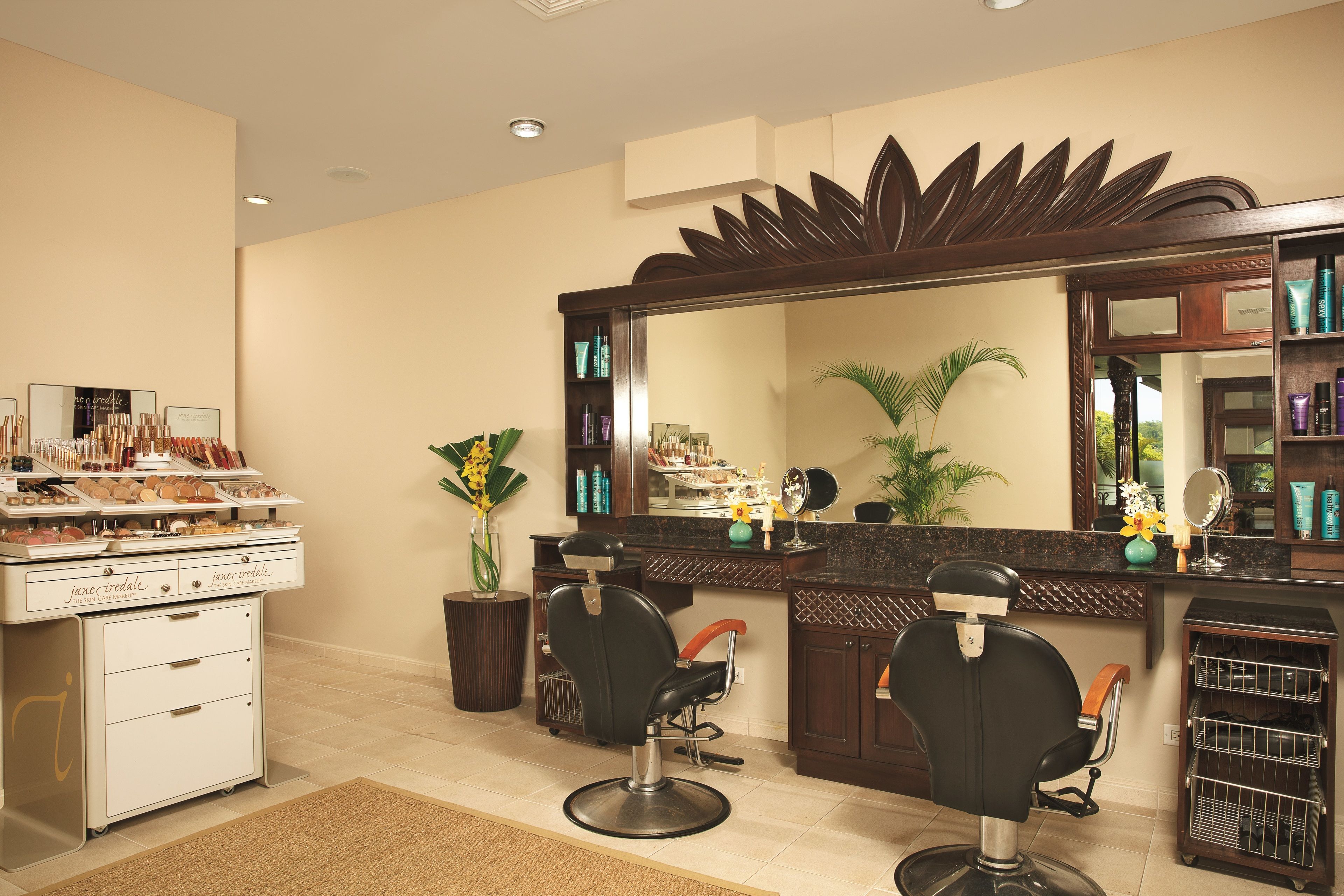 A salon with two black salon chairs, a large mirror, and shelves with hair products.
