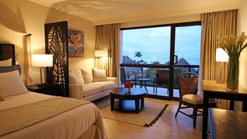 Habitación de hotel con cama, sofá, mesa de centro, sillón, escritorio y vistas al exterior.