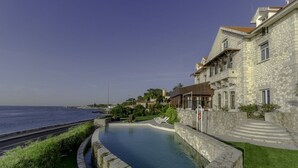 A stone building with a swimming pool, a view of the sea, and a paved walkway. - The Boutique Hotel Solar Palmeiras (Oeiras)