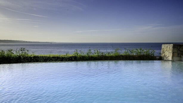 A clear view of a swimming pool with a stone structure on the right and a view of the sea. - The Boutique Hotel Solar Palmeiras (Oeiras)
