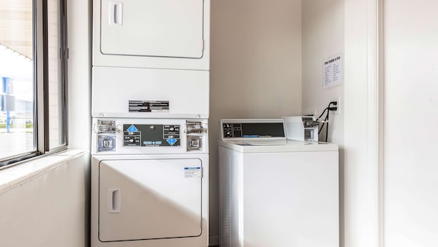 A laundry area with stacked washers and dryers, a window, and a wall-mounted sign. - Motel 6 Tremonton, UT (Tremonton)