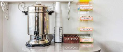 A kitchenette with a coffee pot, a white mug, and a shelf with labeled containers of creamer, sugar, and splenda.