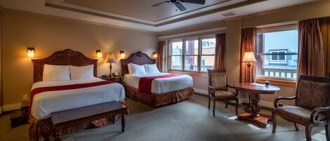 A hotel room with two beds, a ceiling fan, a small table, and a chair.